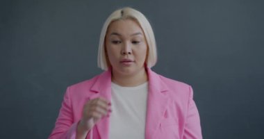 Düşünceli Asyalı kadının yavaş hareket eden portresi sonra parmağını kaldırıp gülümsemesi gri arka planda harika bir fikir olduğunu gösteriyor.