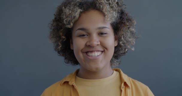 灰色の背景に沈黙を求める指の笑顔で唇に触れる幸せなアフリカ系アメリカ人の女性のクローズアップ遅い動きの肖像画 — ストック動画