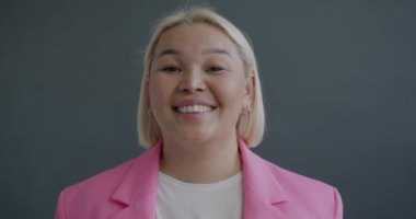 Gri arka planda kameraya gülümseyen başarılı Asyalı iş kadınının yavaş çekim portresi. Halk ve iş kavramı.