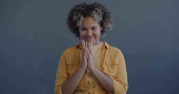 邪恶的年轻非洲裔美国女人的慢动作肖像 她计划用灰色背景的相机揉搓双手 — 图库视频影像