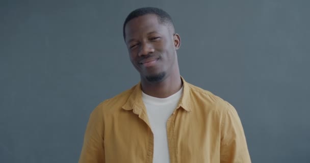 カリスマ的なアフリカ系アメリカ人男性のゆっくりとした動きの肖像画は 灰色の背景のカメラを見ながら微笑みを浮かべます 関係とロマンスのコンセプト — ストック動画