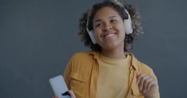 Yavaş çekimde, kulaklıkla müzik dinleyen Afro-Amerikan bayan akıllı telefon tutarak dans ediyor. İnsanlar ve modern teknoloji kavramı.