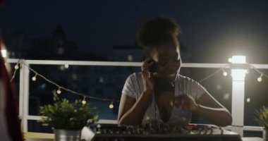 Kaygısız Afrikalı Amerikalı kadın gece açık havada müziğin keyfini çıkarırken ses ekipmanlarıyla dans edip şarkı söylüyor. Yaratıcı etkinlik ve çatı partisi konsepti.