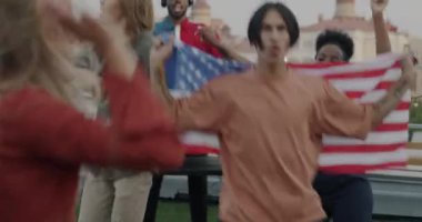 Amerikan bayrağıyla dans eden bir grup genç çatıdaki partide ulusal bayramı kutluyor. Vatanseverler ve modern yaşam tarzı konsepti.