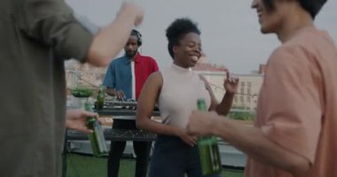 Çatıdaki partide dans eden, kameraya bakıp arkadaşlarıyla müzik dinleyen güzel Afrikalı Amerikalı kadın portresi. Kutlama ve mutluluk kavramı.