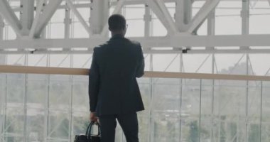 Havaalanında panoramik pencereye karşı duran ve kentsel manzarayı izleyen takım elbiseli iş adamlarının arka görüntüsü. İş seyahati ve iş dünyası kavramı.