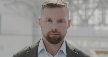 Modern ofis lobisinde durup kameraya bakan ciddi genç girişimcinin yavaş çekim portresi. Başarılı bir kariyer ve mesleki meslek kavramı.