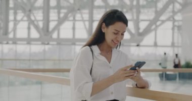 Akıllı telefon kullanarak modern cam duvar ofis binasında duran hırslı yöneticinin yavaş çekim portresi. Teknoloji ve başarılı insanlar konsepti.