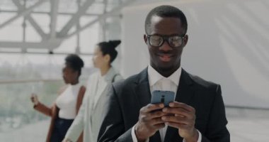Yenilikçi ofis lobisinde akıllı telefon kullanarak yakışıklı Afro-Amerikan müdürün yavaş çekimde portresi. İletişim ve teknoloji kavramı.