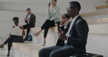 Mutlu Afrikalı Amerikalı işadamı cep telefonuyla konuşuyor ve ofis binasının yanındaki merdivenlerde baş parmak gösteriyor. İletişim ve iyi haber kavramı.