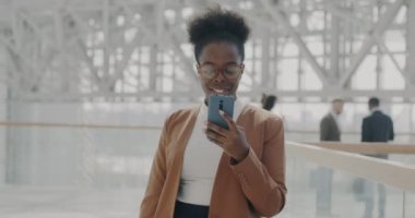 Akıllı telefon kullanan başarılı genç iş kadınının yavaş çekimde portresi ofis binasının lobisinde kurumsal iletişimin keyfini çıkarıyor.