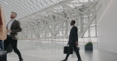 Modern havaalanında çanta taşıyan iş adamlarının ve kadınların ağır çekimde yürümesi. İş gezilerine giderken resmi kıyafetler giyen yolcular..