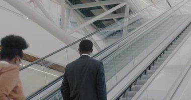 Çağdaş havaalanı binasında yürüyen merdivenle yürüyen yavaş çekim ekibi gezinin tadını çıkarıyor. Takım çalışması ve işe gidip gelme kavramı.