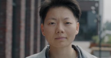 Şehir sokaklarında gülümseyen neşeli Asyalı adamın hafif bir gülümseme ile kameraya bakışının yavaş çekim portresi. Duygu ve şehir insanı kavramı.