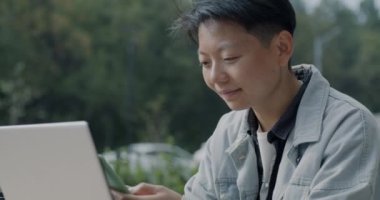 Başarılı Asyalı serbest çalışan akıllı telefon konuşmaları yapıyor ve şehirdeki bir kafede dizüstü bilgisayarla çalışıyor. Modern aletler ve milenyum konsepti.