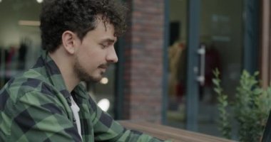 Orta Doğulu bir öğrencinin diz üstü bilgisayarla çalıştığı eğik portresi sokak kafesinde uzak eğitime odaklanmış. E-öğrenme ve kentsel yaşam tarzı kavramı.