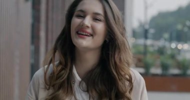 Neşeli genç bir kadının yavaş çekimde çekilmiş portresi. Şehrin dışında kameraya bakarak neşe ifade ediyor. Mutluluk ve insan kavramı.