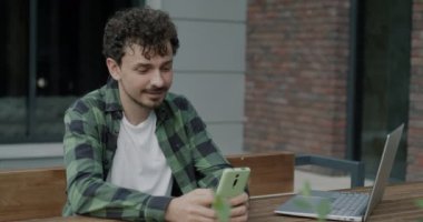 Orta Doğulu bir öğrenci internette sörf yaparken gülümsüyor ve şehirdeki bir kafede dizüstü bilgisayarla oturuyor. Modern alet ve şehir yaşam tarzı konsepti.