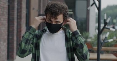 Orta Doğulu bir adamın yüz maskesi takan portresi ve salgın sırasında şehrin dışında duran kameraya bakıyor. Sağlık ve kentsel yaşam tarzı kavramı.