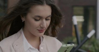 Şehir caddesinde arka planda bulanık duran akıllı telefonuyla mesajlaşan genç bayanın zoom portresi. Gadget ve milenyum konsepti.