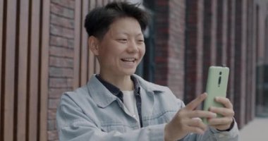 Asyalı adam akıllı telefonuyla online video görüşmesi yapıyor ve şehirde el sallayarak konuşuyor. İnternet iletişimi ve modern aygıtlar kavramı.