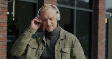 Şehir caddesinde kablosuz kulaklık takmış, müzik dinleyen neşeli bir adam. Kentsel çağlar ve teknoloji kavramı.