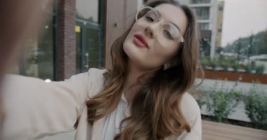 Selfie için poz veren genç bir kadının yavaş çekim portresi. Kameraya bakıyor. Açık havada güzel yüzler yapıyor. Fotoğraf ve insan konsepti.