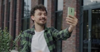 Neşeli Orta Doğulu bir adam şehir sokaklarında arkadaşlarıyla sohbet ederek online video görüşmesi yapıyor. Kentsel yaşam tarzı ve modern teknoloji kavramı.