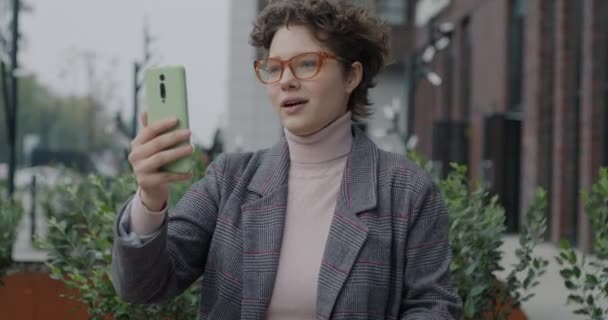 街の通りでスマートフォンカメラを使ってオンラインビデオ通話をする楽しい少女の学生 コミュニケーションとテクノロジーコンセプト — ストック動画