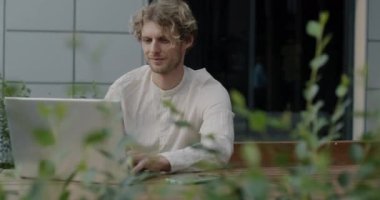 Yaz günü sokak kafesinde oturan, dizüstü bilgisayar kullanan serbest çalışan bir erkek. Profesyonel aktivite ve başarılı serbest çalışanlar konsepti.