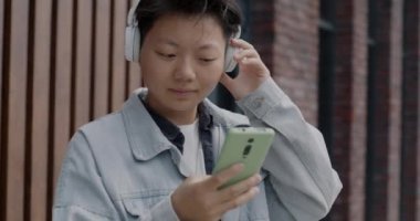 Akıllı telefon kullanan ve kulaklıkla şehir dışında müzik dinleyen kaygısız Asyalı adam. İnsanlar ve modern aletler kavramı.