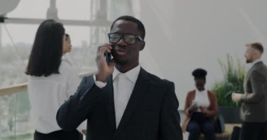 Ofis lobisinde yürüyen ve cep telefonuyla konuşan takım elbiseli işadamının yavaş çekimde çekilmiş resmi. İş iletişimi ve işyeri kavramı.