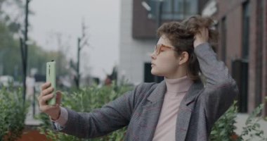 Akıllı telefon kamerası için selfie çeken neşeli genç bir kadın şehirde eğleniyor. Fotoğraf ve milenyum konsepti.