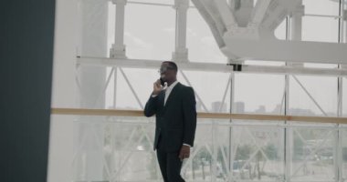 Güzel, modern havaalanında cep telefonuyla konuşan kendinden emin Afrikalı Amerikalı iş adamının yavaş hareketi. Cep telefonu iletişimi ve iş dünyası kavramı.