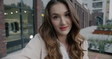 Çevrimiçi video görüşmesi yapan genç bir kadının yavaş çekim portresi. Açık havada gülerek konuşuyor. Sevimli bir bayan kameraya bakıp olumlu duygularını ifade ediyor..