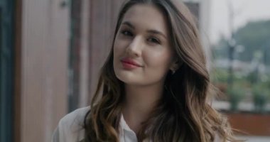 Uzun dalgalı saçlı çekici bir bayanın açık havada hafif bir gülümsemeyle kameraya bakışının yavaş çekim portresi. İnsanlar ve olumlu duygu kavramı.