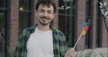 Orta Doğulu genç bir adam elinde Alman bayrağıyla kameraya bakıp gülümsüyor. Seyahat ve göç kavramı.