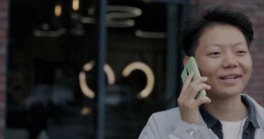 Meşgul şehir caddesinde cep telefonuyla konuşan neşeli Asyalı kişinin portresi. Cep telefonu iletişimi ve şehir yaşam tarzı kavramı.