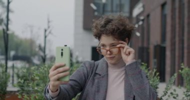 Modern şehirde sosyal medya için selfie çeken neşeli genç bayanın yavaş çekimleri. Fotoğraf ve Etkilenenler konsepti.