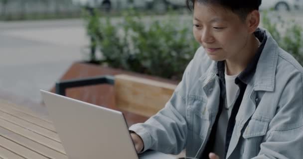 亚洲男子自由职业工人坐在城市室外咖啡馆里 用笔记本电脑打字 动作缓慢 现代技术和自由职业概念 — 图库视频影像