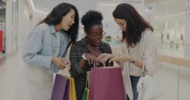 Bir grup genç bayan arkadaş alışveriş merkezindeki alışveriş poşetlerinde konuşuyorlar ve alışverişe bakıyorlar. Dostluk ve tüketim kavramı.