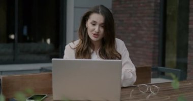 Sokakta, kafede dizüstü bilgisayarla konuşan duygusal genç bir kadının portresi. İş iletişimi ve insan kavramı.