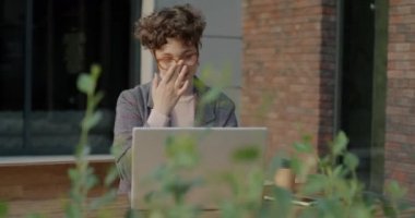 Şen şakrak öğrenci dizüstü bilgisayarla çalışıyor. Yazıyor ve akıllı telefon kullanıyor. Kentteki açık kafede oturuyor. Teknoloji ve çevrimiçi eğitim konsepti.