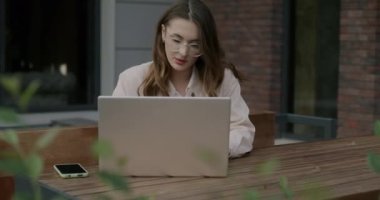 Dizüstü bilgisayarla çalışan kız öğrenci sokak kafesinde online eğitime odaklanmış. E-öğrenme ve gençlik yaşam tarzı konsepti.