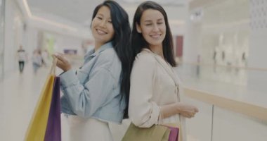 Modern alışveriş merkezinde kameraya gülümseyen genç bayan arkadaşlarının yavaş çekimde portresi. İş ve tatmin olmuş müşteri kavramı.