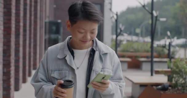 Zpomalení Pohybu Bezstarostný Asijský Student Chůze Venku Pomocí Smartphonu Pití — Stock video