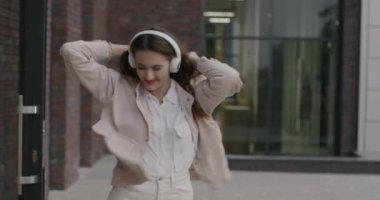 Yavaş çekimde, kulaklık takan, dans eden, müzik dinleyen şehir sokaklarında gezen neşeli genç bayanın portresi. Gençlik kültürü ve modern yaşam tarzı kavramı.