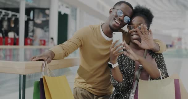 ショッピングモールでバーチャルミーティングを楽しむオンラインビデオ通話中に男と男が話して手を振る スマートフォンや紙袋を持っている人 — ストック動画