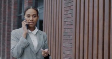 Afrika kökenli Amerikalı bir kadının cep telefonuyla konuşması şehir merkezinin önünde yürürken. Profesyonel iletişim ve modern iş konsepti.