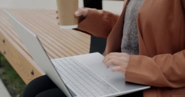Orta Doğulu bir kadının diz üstü bilgisayarla çalışıp kulaklıkla müzik dinlerken ve dışarıda kahve içerken çekilmiş bir portresi. Modern teknoloji ve gençlik yaşam tarzı kavramı.